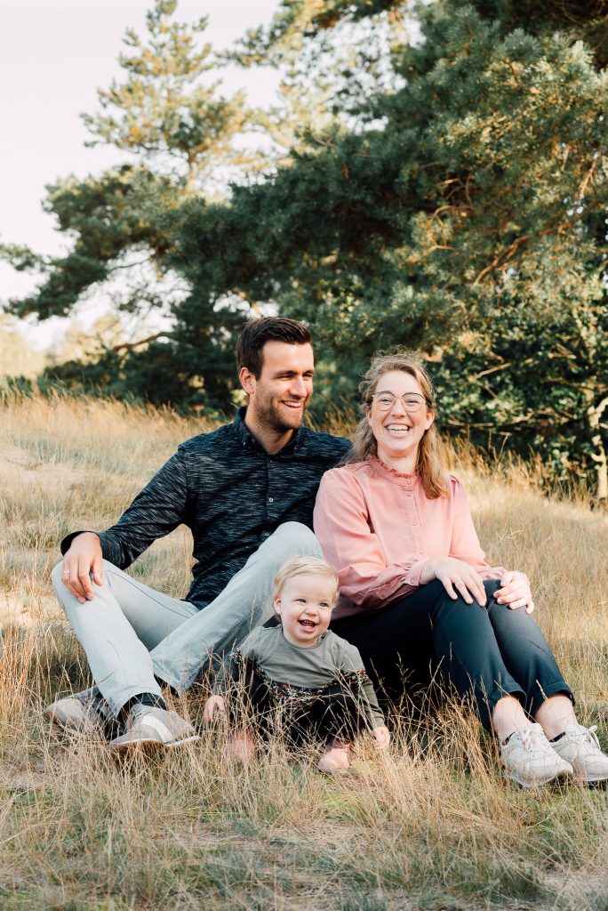 Familie van drie midden in de natuur. Ze lachen naar elkaar terwijl ze elkaar liefdevol vasthouden.