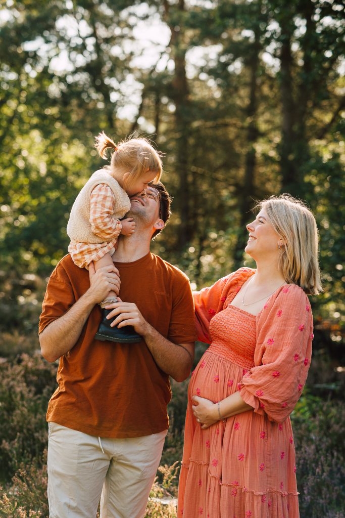 Jong gezin staat midden in de natuur en kijken elkaar glimlachend aan tijdens de familiefotoshoot in Arnhem