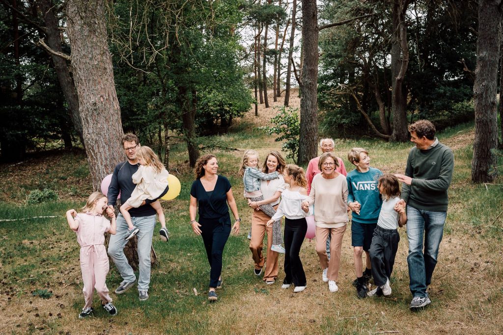 grote hectische familie loopt naast elkaar richting de camera tijdens een familiefotoshoot in het bos van Arnhem.