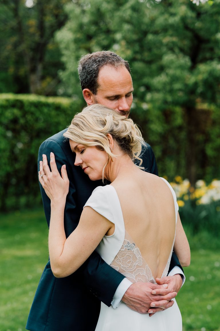 Een liefdevolle foto van een bruidspaar dat elkaar vasthoud terwijl ze de ogen dichthouden. Ze staan in de natuur tijdens hun bruiloft